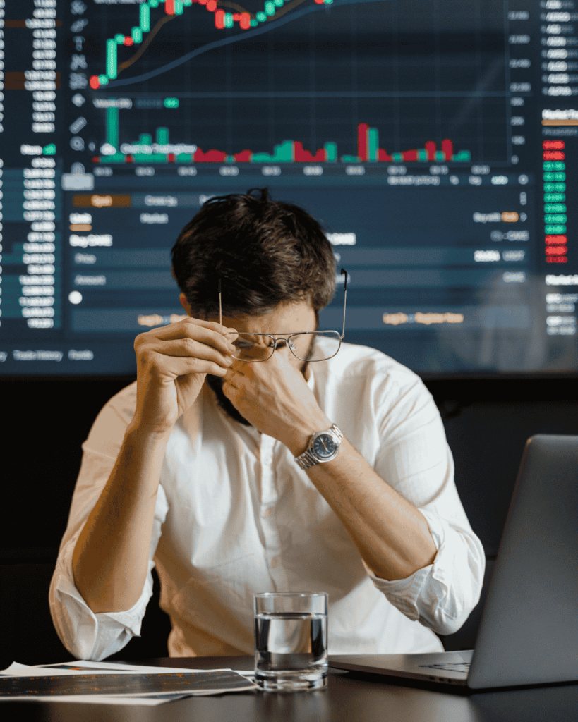 Gestresster Mann reibt sich die Augen und hält eine Brille. Im Hintergrund ein Trading Chart itcoin Starter